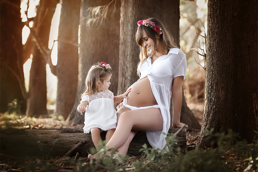 Hermoso momento, la caricia de su hermana mayor en la panza de la mamá. Ambas sentadas sobre un tronco una tarde cálidos, disfrutando de sus mimos. Barby Massei Fotografía, Sesión Maternidad.