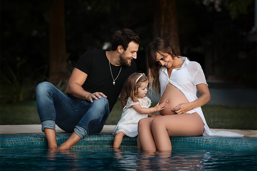 Familia disfrutando al aire libre, una bello día de verano. Mamá, papá y su hermanita. Ellas con sus vestidos blancos y el papá con su jeans y remera negra. Caricias, mimos, y mucha alegría. Barby Massei fotógrafa. Sesión familiar. Maternidad en familia. 