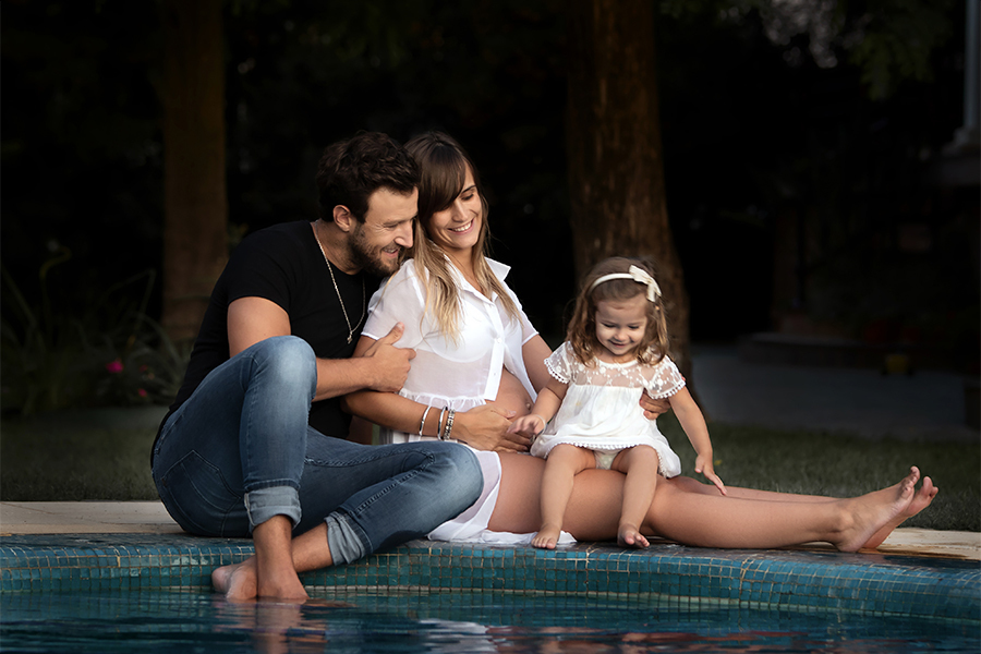 Esperando con mucho amor la llegada de su segundo hijo, papá, mamá y su hermanita, al lado de pileta, disfrutando de un bello atarceder. Barby Massei fotógrafa, sesión familiar.
