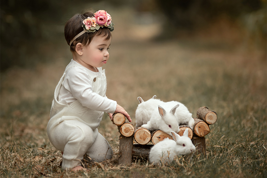 Niña con enterito blanco jugando con conejitos en el campo al atardecer.