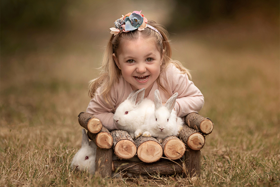 Niña con corona de flores y conejos blancos. Granja para el book de fotos de Mía. Barby Massei fotografía