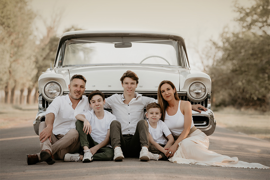 Familia posando para el book de fotos al atardecer en el campo en Santa Fe. Vestidos de blanco con auto de colección. Barby Massei fotografía