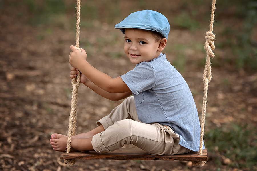 Niño con boina celeste en la hamaca de madera. Sesión para el book infantil de Barby Massei.