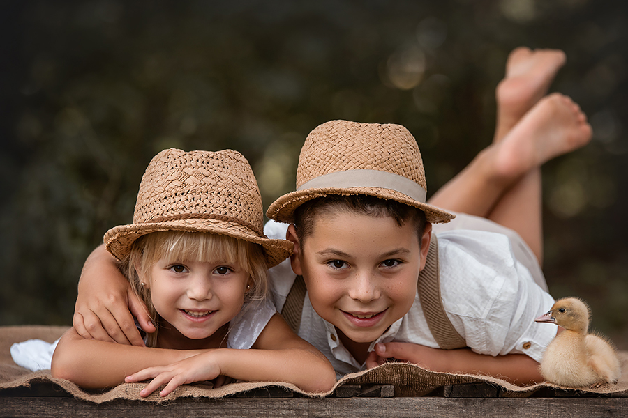 Hermanitos en la sesión de fotos en el campo en Santa Fe. Niños vestidos de blanco con sombrero de paja. Barby Massei