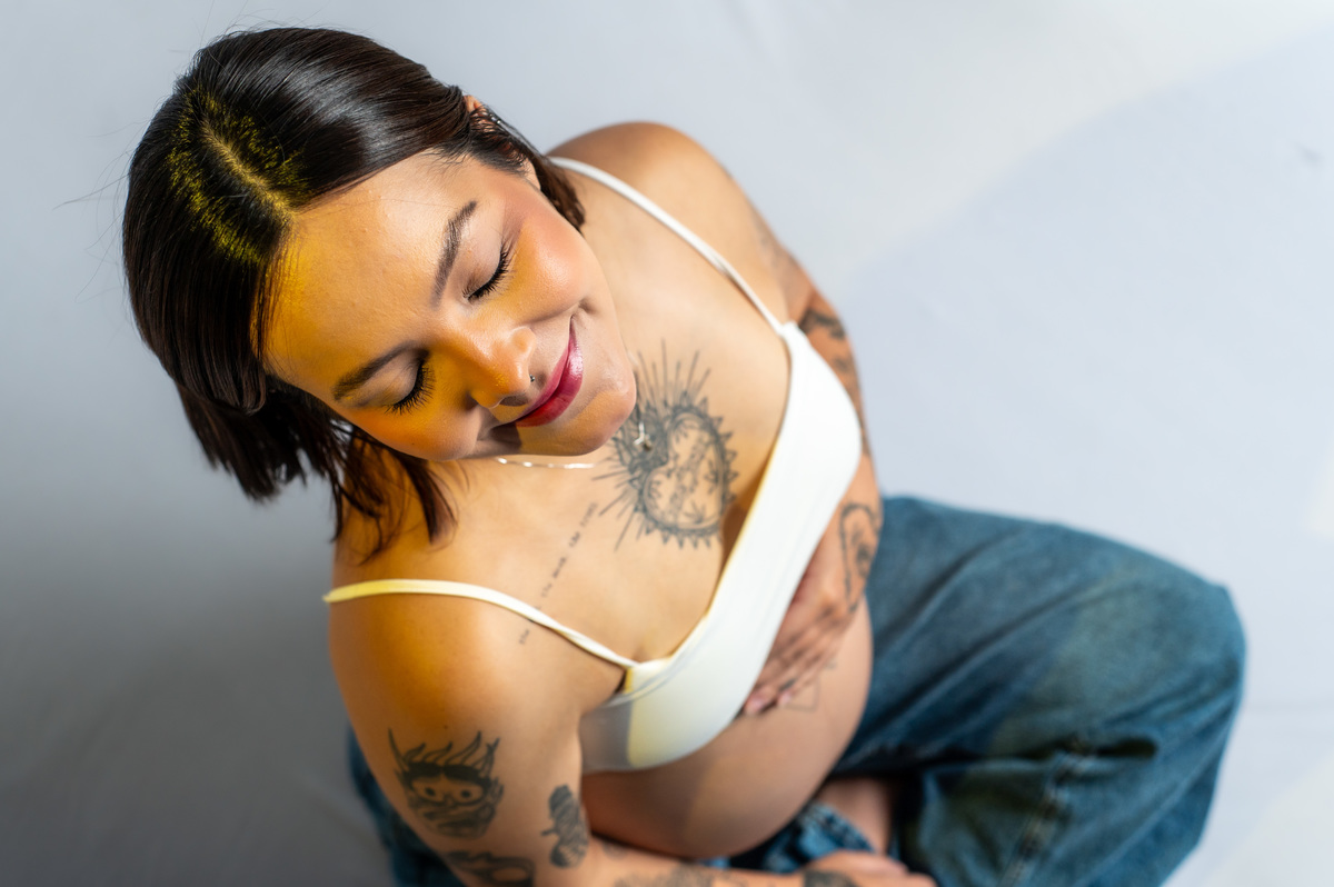 Retrato de gestante com expressão serena, luz suave e destaque para a barriga, ensaio delicado e sensível de maternidade.