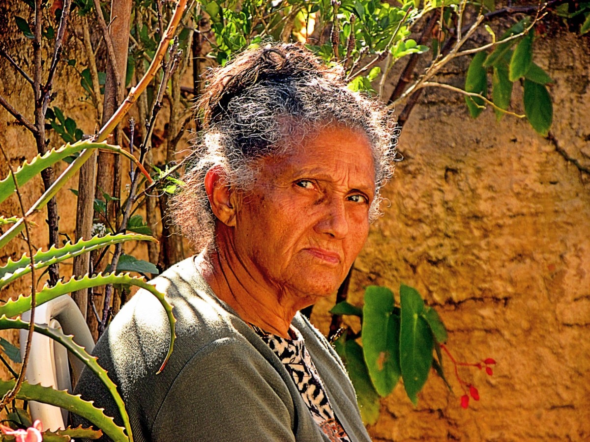 A senhora de cabelos brancos, sentada, observa atentamento a câmera fazer o clique. No seu olhar pensamentos passeiam e, ao redor, o tempo vai passando.
