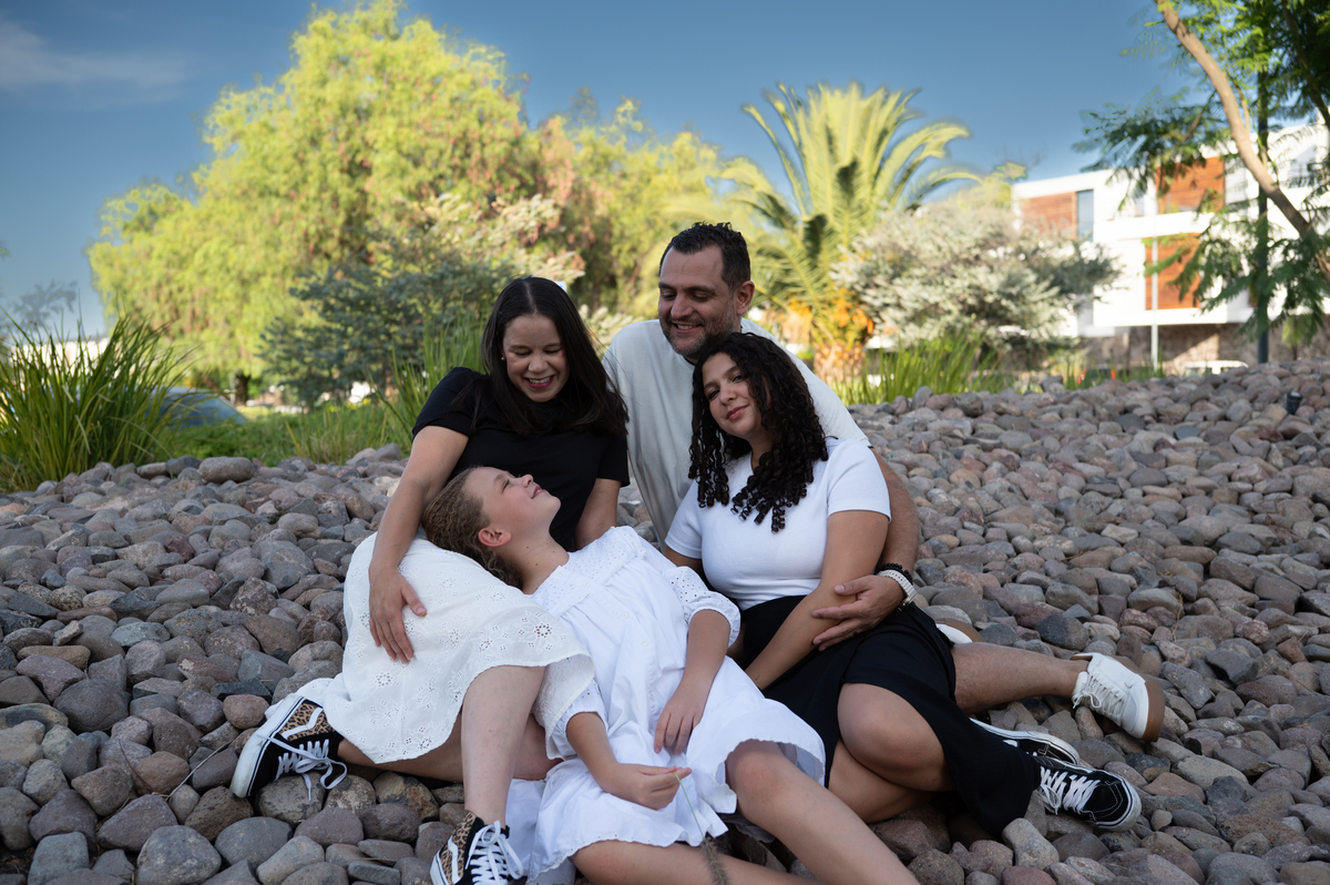 La familia disfruta un momento tranquilo sentada sobre las piedras de un parque en Querétaro. Un retrato lifestyle que resalta la cercanía entre padres e hijas en un entorno natural.