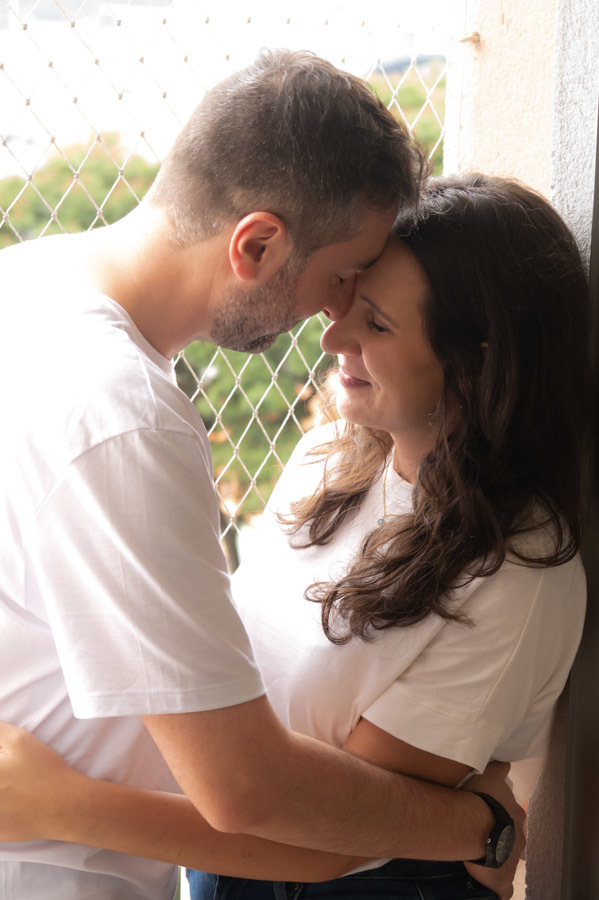Lucas besando la frente de Cami junto a la ventana de su casa. Sesión de preboda con luz natural en Querétaro.