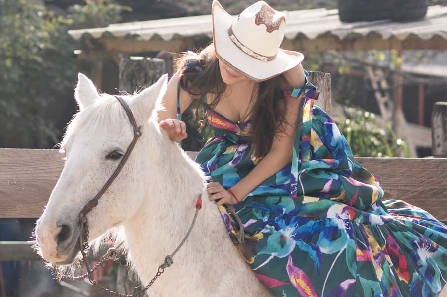 quinceañera con sombrero vaquero recargada en su caballo blanco