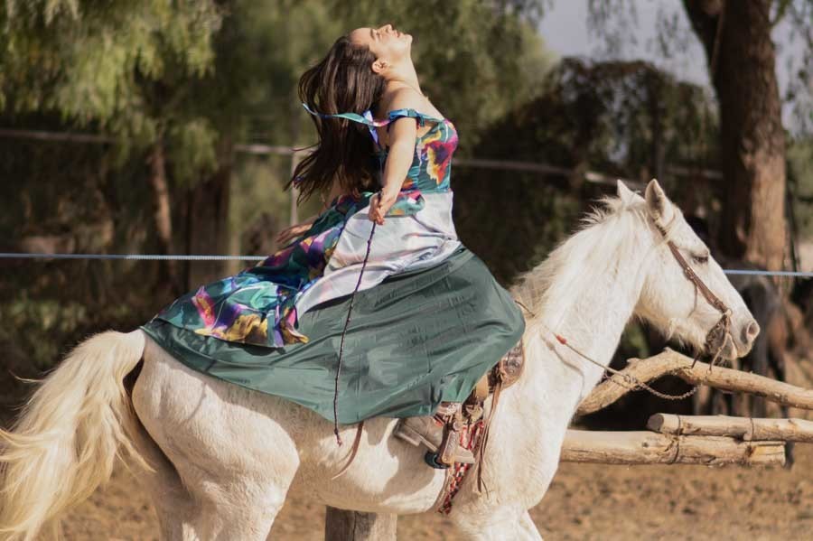 Quinceañera cabalgando con vestido de XV años extendido sobre un caballo blanco