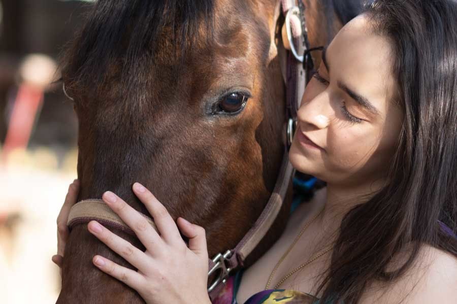Sesión de XV años: quinceañera abrazando la cara de su caballo café