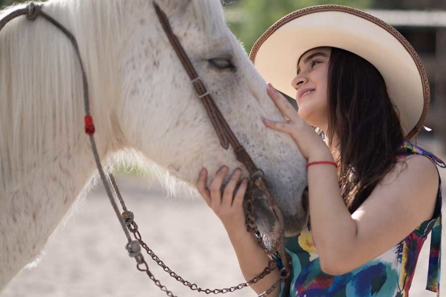 Quinceañera con sombrero vaquero frente a frente con un caballo blanco, sesión de XV años con caballos