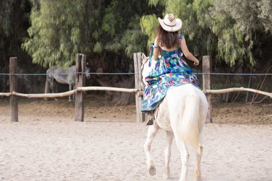 Sesión de XV años con la quinceañera cabalgando en la arena con sombrero vaquero