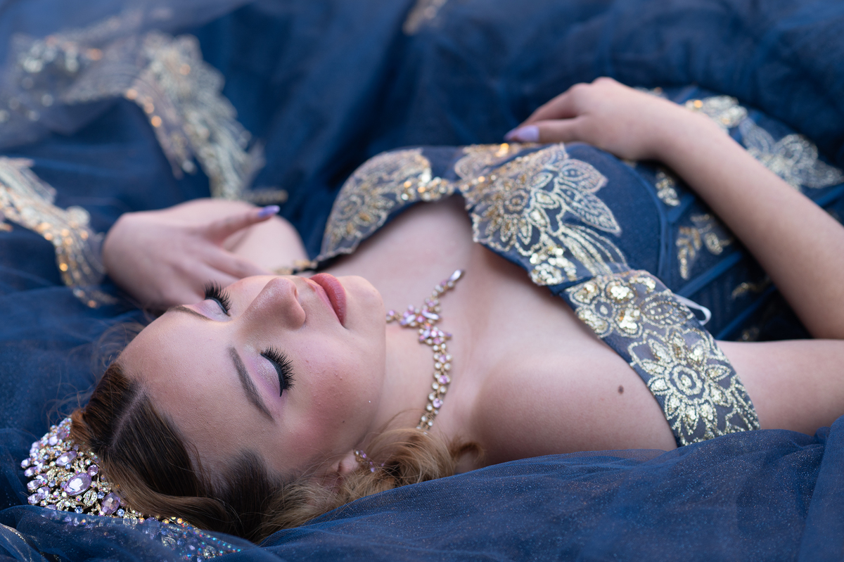 Quinceañera recostada con vestido azul y dorado, retrato de XV años desde arriba