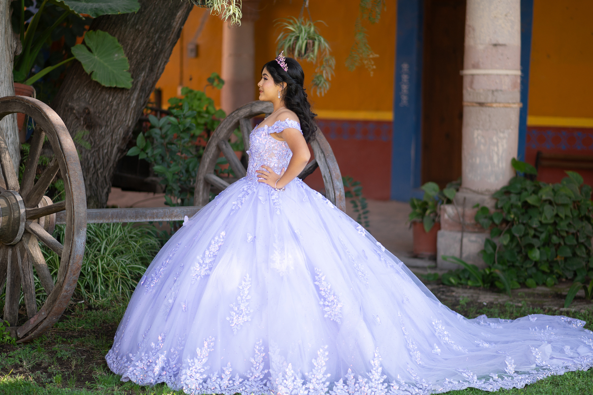 Vestido de XV años lila junto a una carreta antigua en un espacio campestre