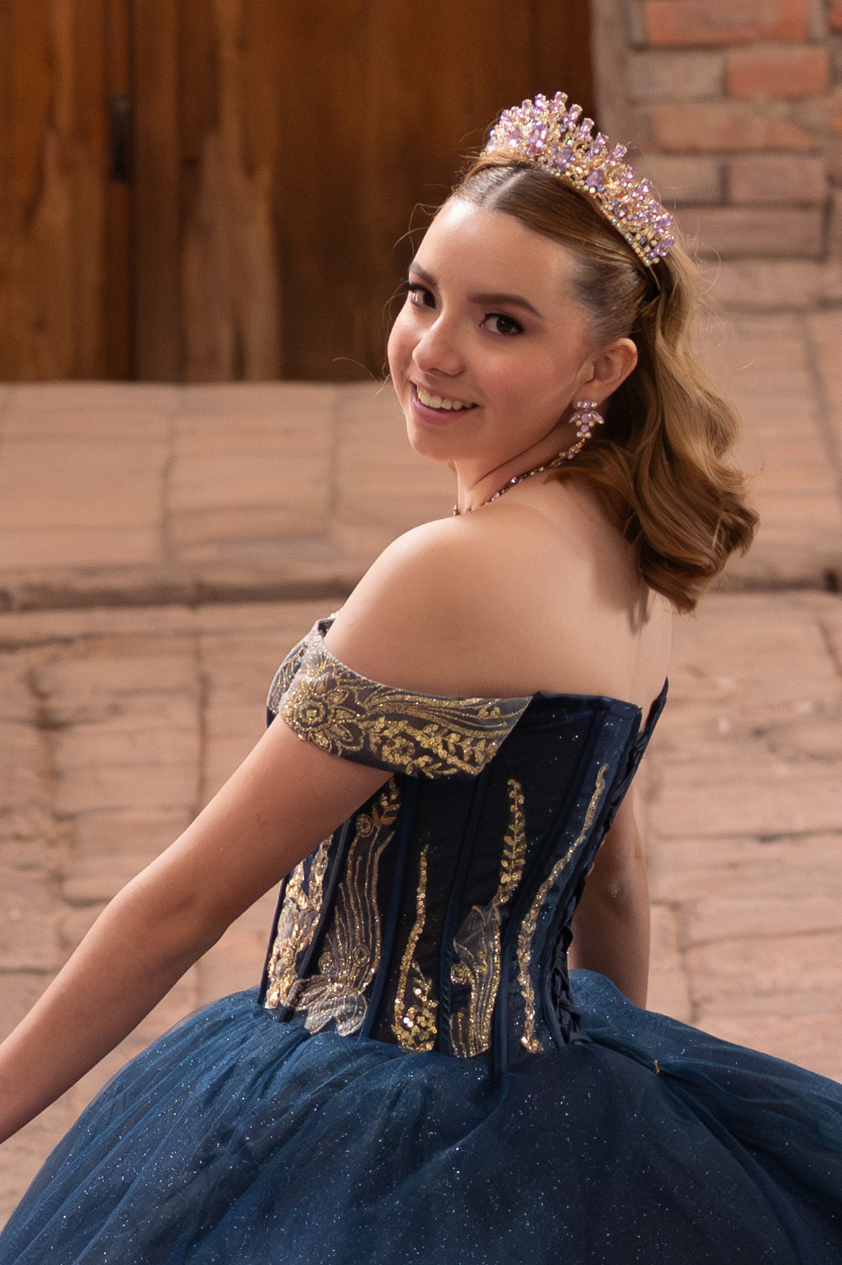 Quinceañera con vestido azul marino y corona junto a una puerta de madera antigua