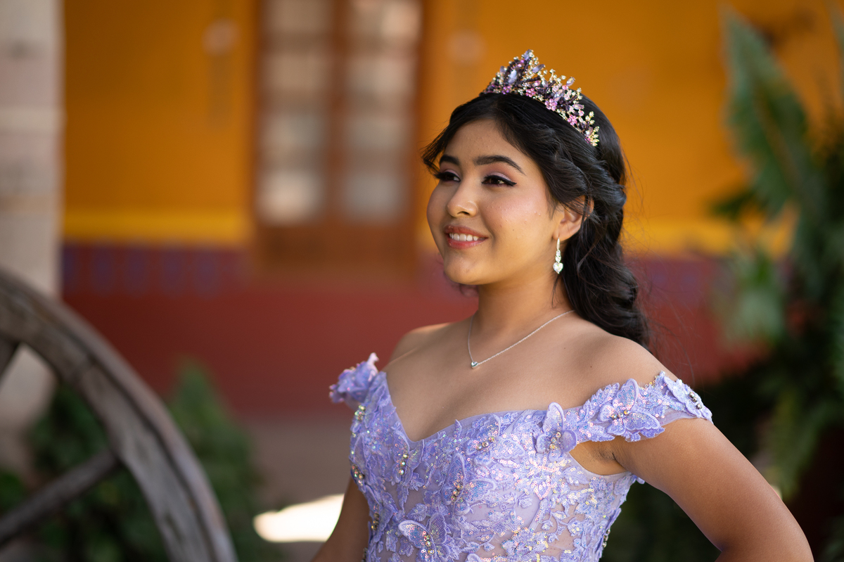 Quinceañera con vestido de XV años lila frente a un muro amarillo de hacienda