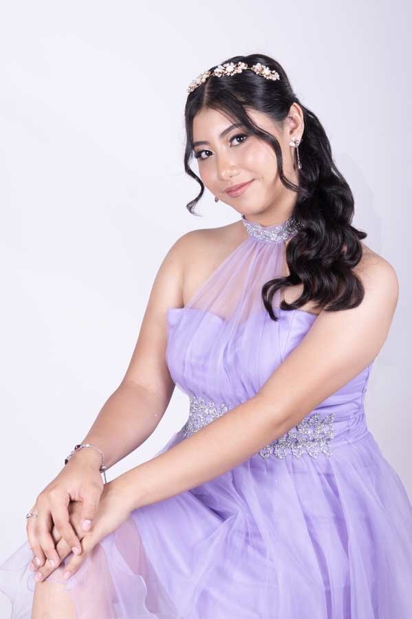 Quinceañera sentada con vestido lila de XV años sobre fondo blanco en estudio