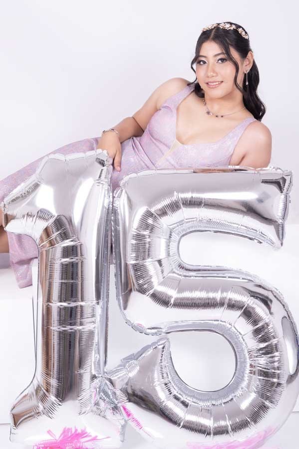 Quinceañera sentada sobre globos plateados del número 15, sesión de XV años en estudio 