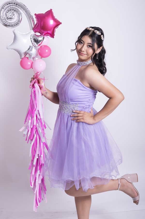 Quinceañera con vestido lila saltando junto a globos rosas, sesión de XV años en estudio fotográfico