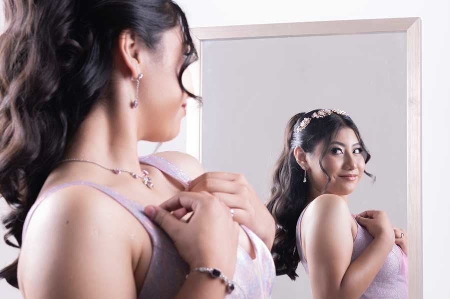 Quinceañera arreglándose frente al espejo en su sesión de XV años en estudio