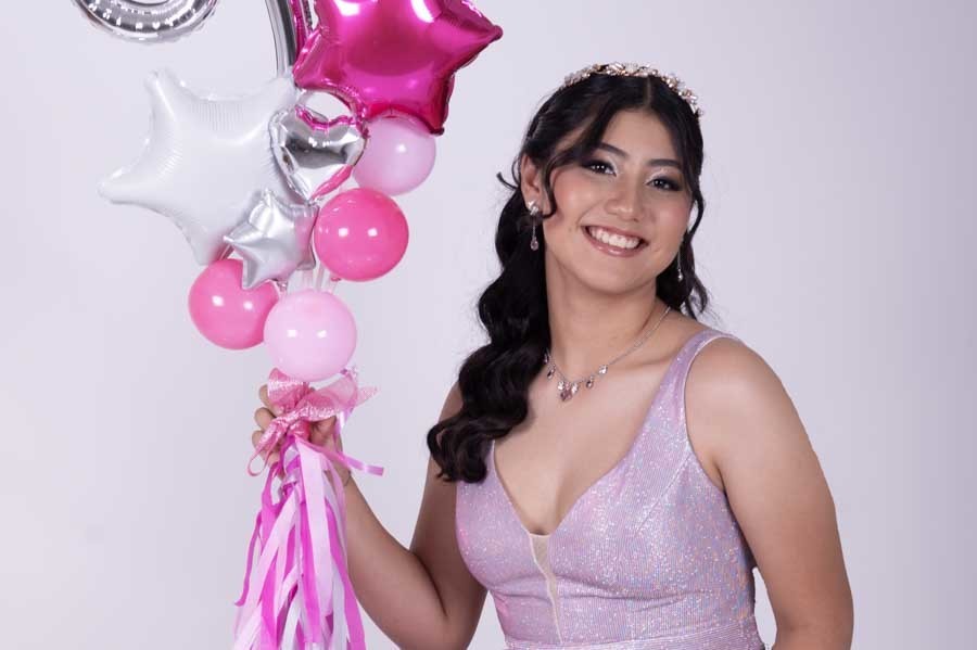 Quinceañera sonriendo junto a globos rosas y plateados, sesión de XV años