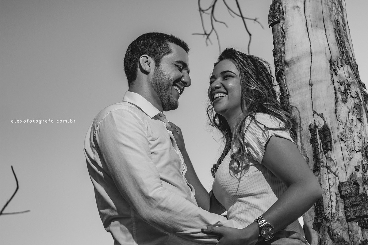 Noivos encostados em árvore, sorrindo felizes. Um momento de muita descontração e alegria na prévia do casal