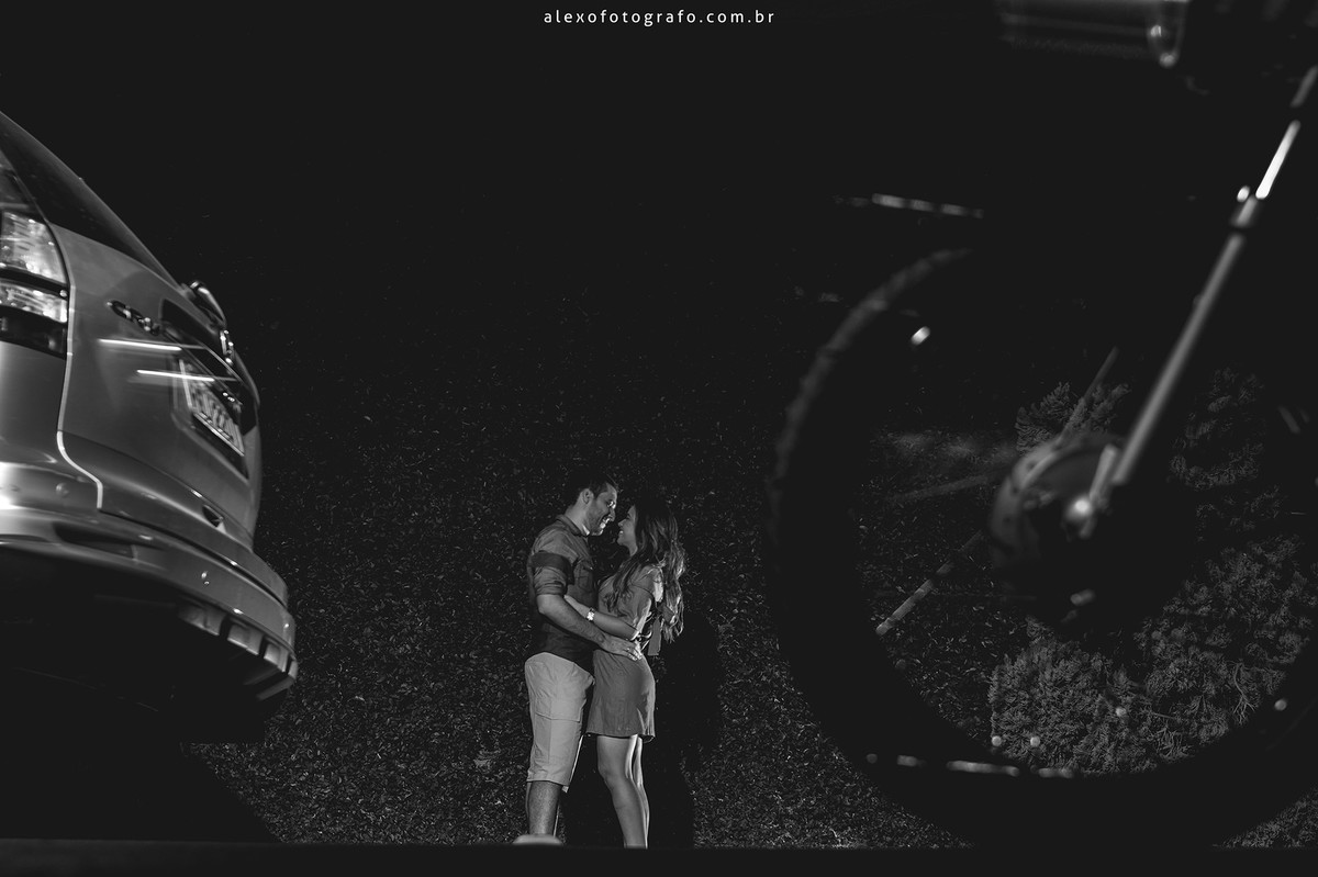 foto preto e branco dos noivos num paredão de plantas no trânsito com carros e motos passando