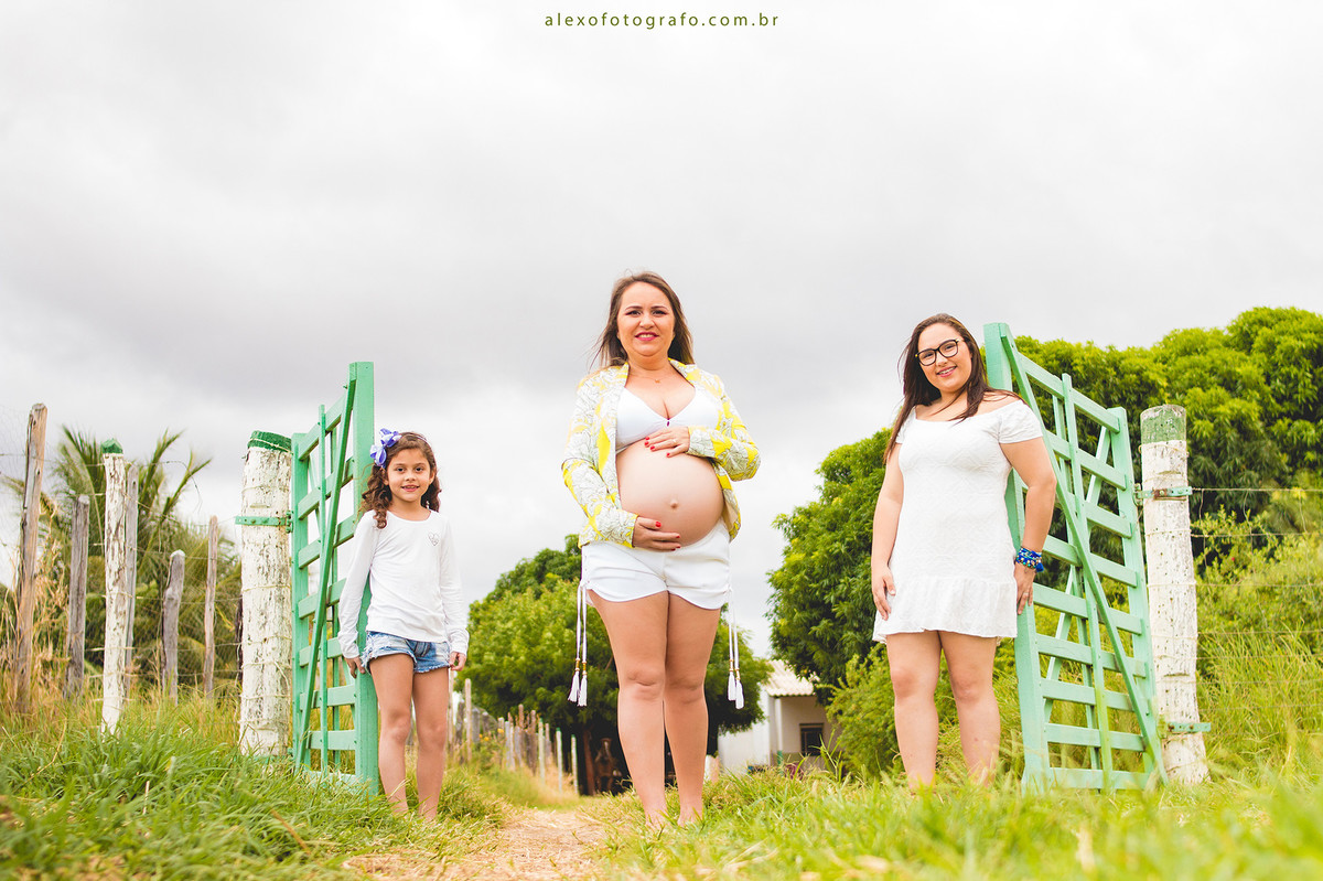 gestante com as filhas na porteira na paisagem do campo lindo ensaio externo de grávida