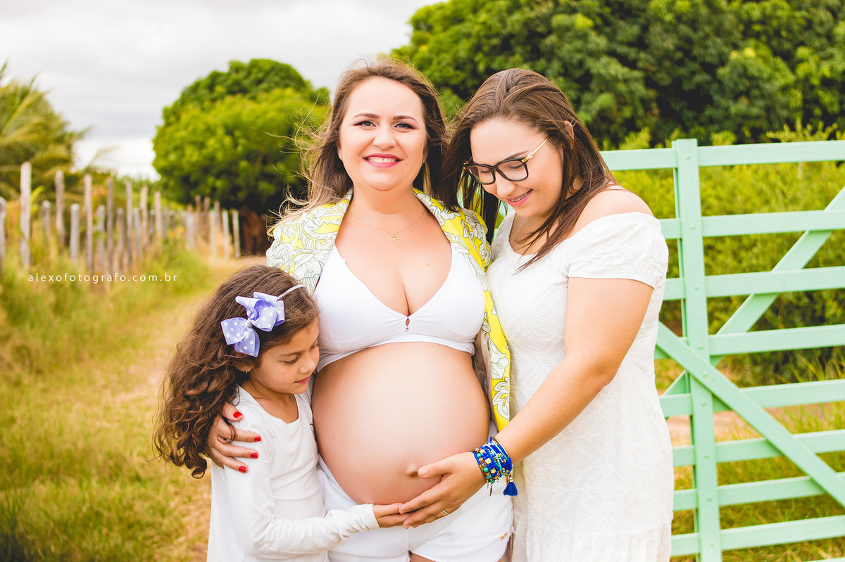 gestante com as filhas na porteira na paisagem do campo lindo ensaio externo de grávida