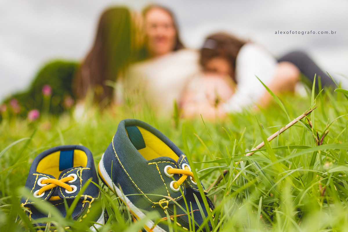 ensaio de gestante sentada na grama com as filhas e foco nos sapatinhos