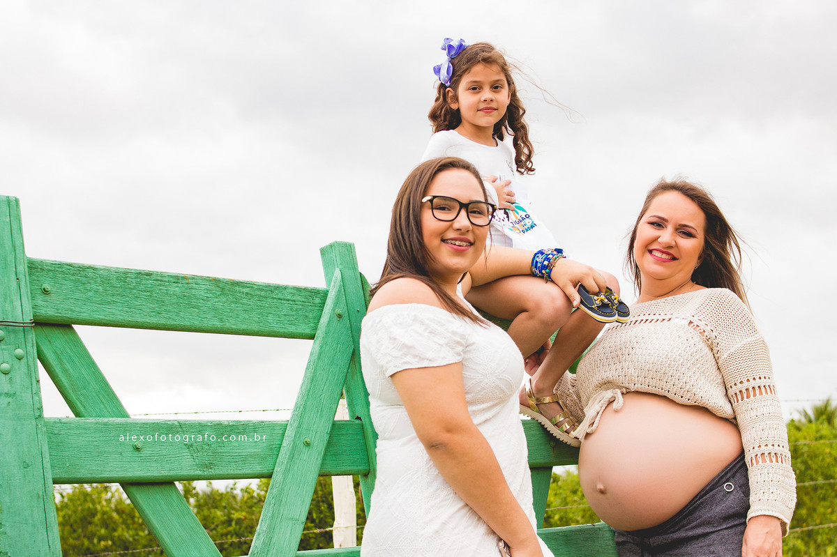 gestante com as filhas na porteira na paisagem do campo lindo ensaio externo de grávida