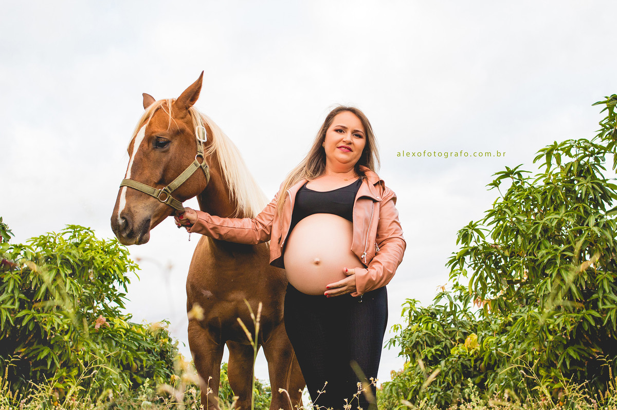 ensaio de gestante no meio da plantação de acerolas vestida de vaqueira segurando uma égua e com a outra mão na barriga