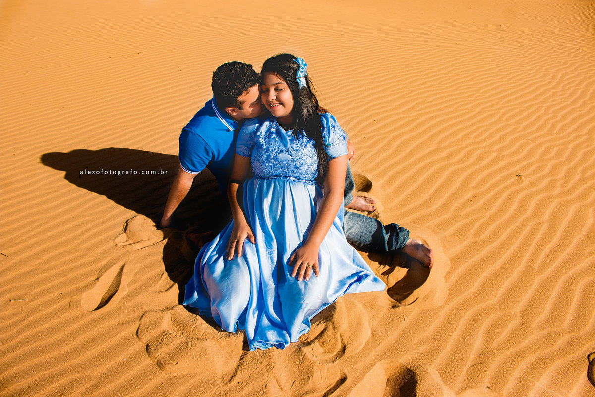 ensaio de gestante, casal sentado na areia das dunas de casa nova, o marido dando um xero na esposa grávida