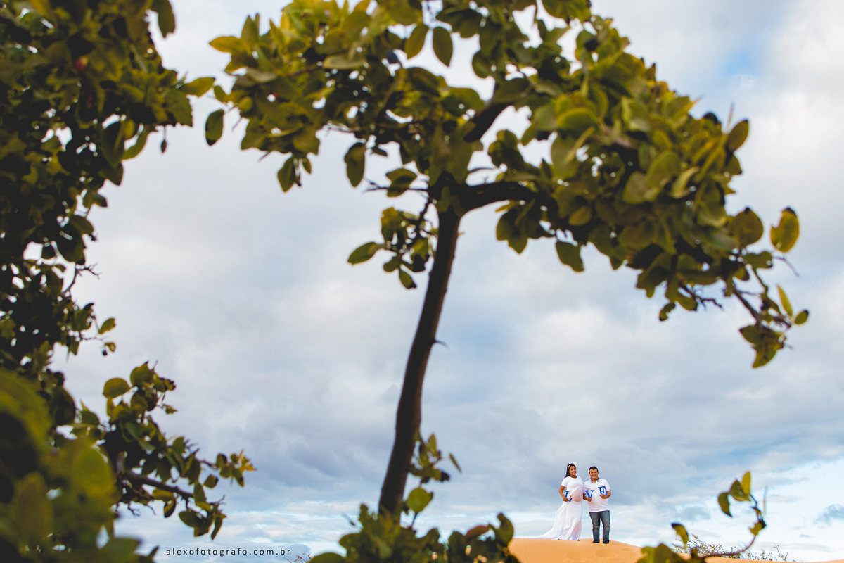 ensaio de gestante, casal de pé na duna em casa nova segurando o nome love onde o o da palavra é a barriga da mulher grávida