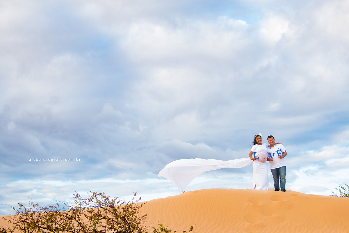 ensaio de gestante, casal de pé na duna em casa nova segurando o nome love onde o o da palavra é a barriga da mulher grávida