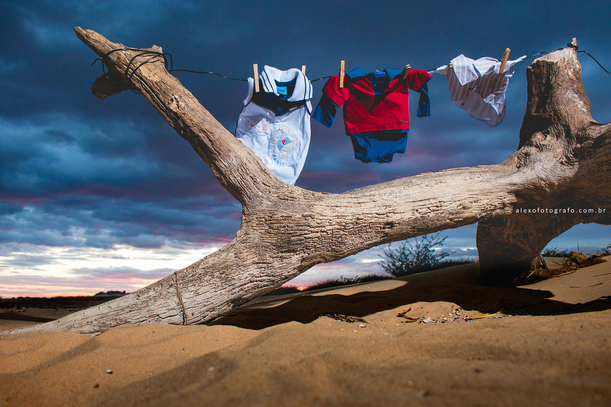 ensaio de gestante, varal de roupinhas do bebê num galho no chão e o céu azul ao fundo