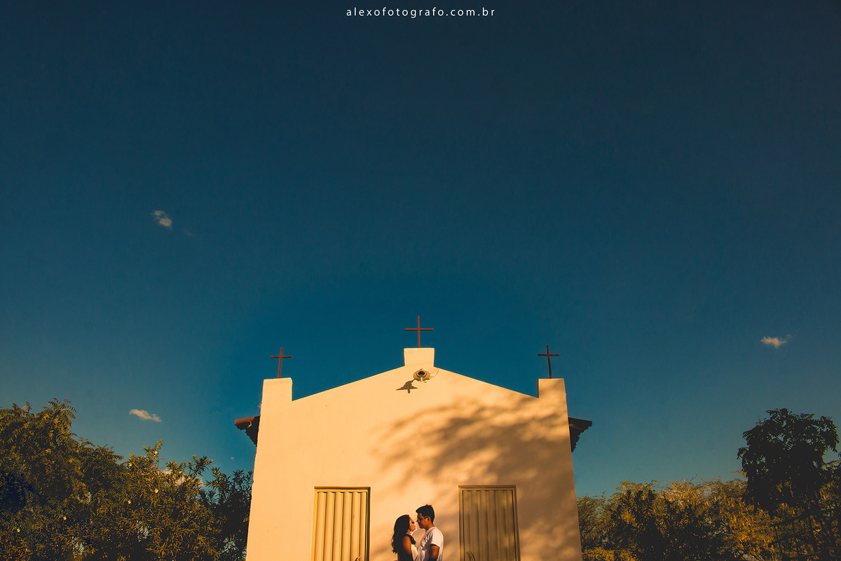 noivos em frente a uma igreja do interior com três cruzes no topo. Foto meio corpo dos noivos se olhando e bastante céu. fotografia de composição