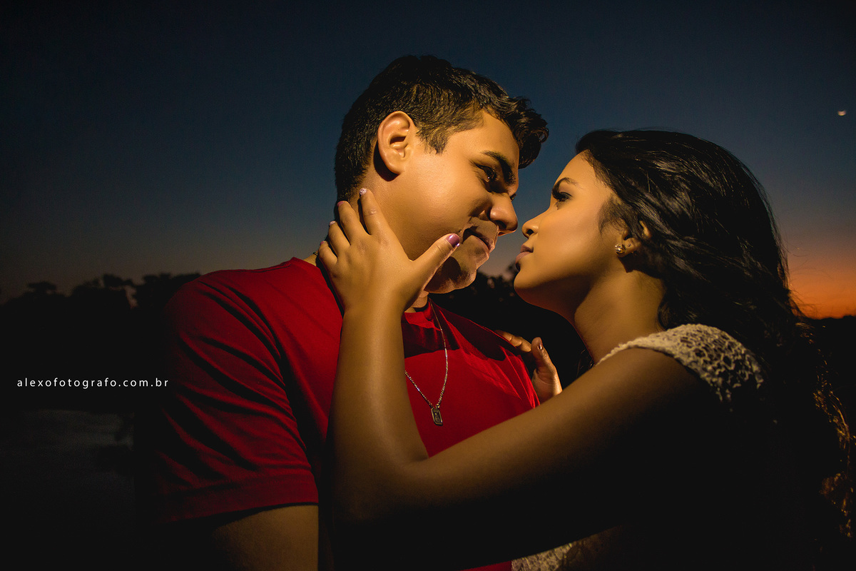 Noivos se olhando enquanto a noiva pega no rosto do noivo. foto feita no final da tarde depois do pôr do sol e com luz de celulares.