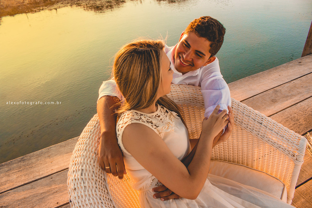 casal no pie, noiva sentada numa poltrona de fibra e o noivo por trás da poltrona com os braços em volta da sua noiva e ambos se olhando