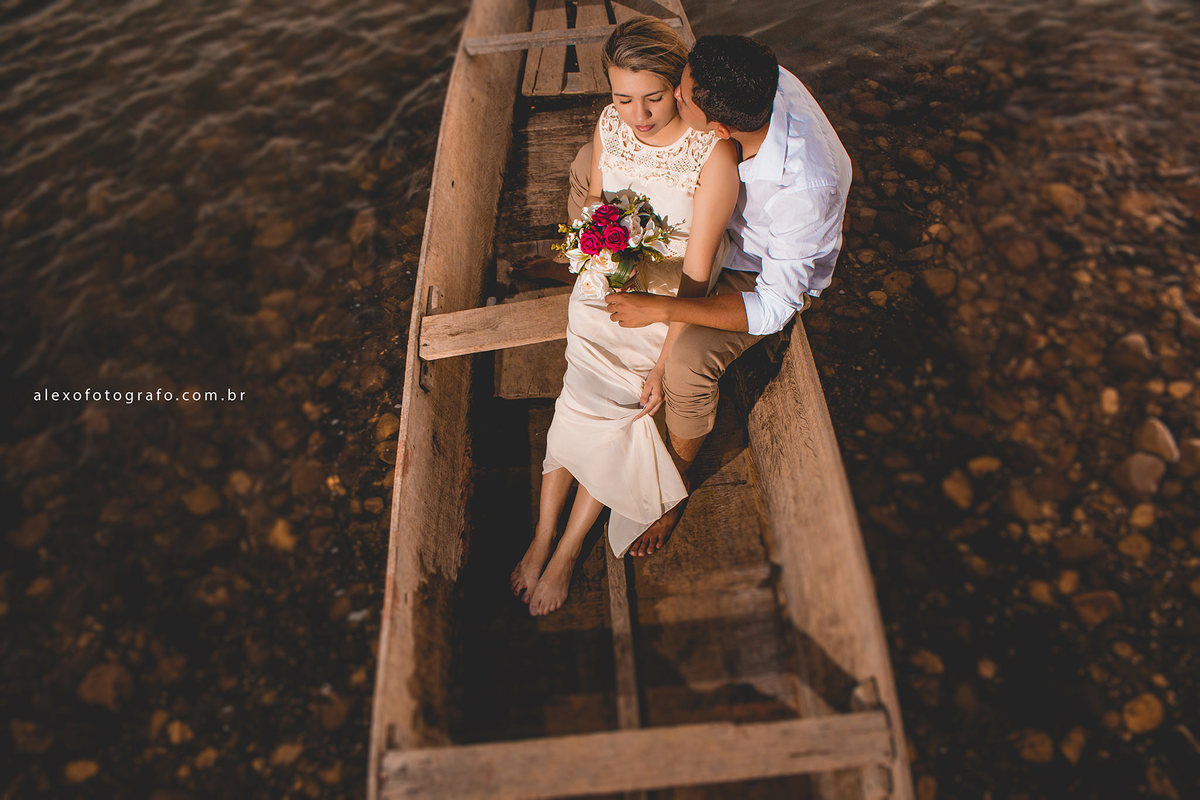 casal sentado num barco velho a margem do  rio são francisco abraçados e segurando um buquê de flores