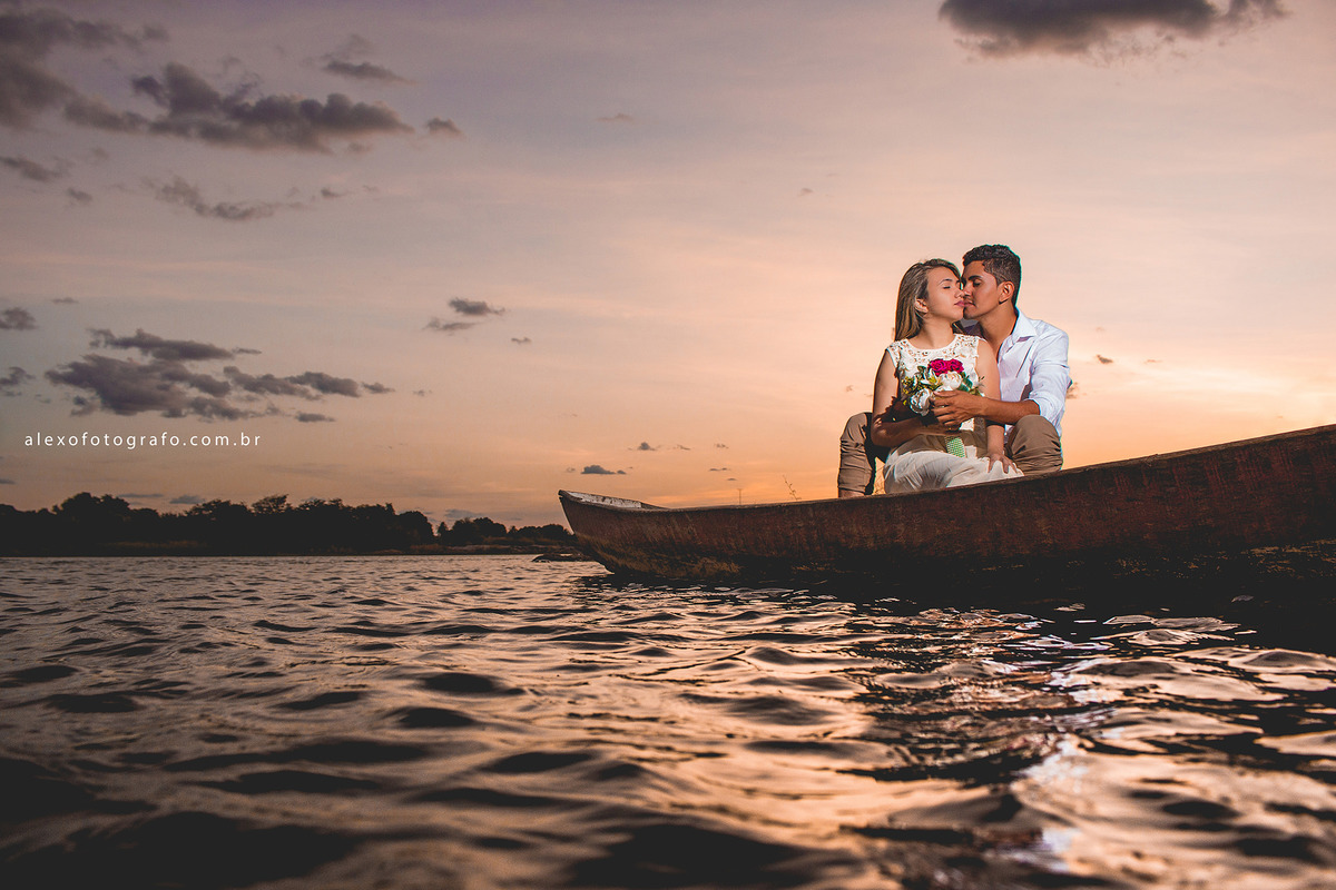 casal sentado no barco ao pôr do sol, noivo dando um xero nos zói