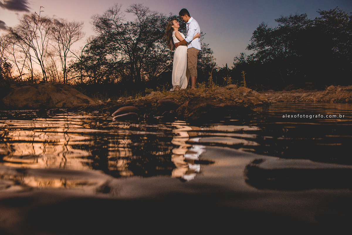 casal abraçado ao pôr do sol se olhando. Foto pegando bastante a água 