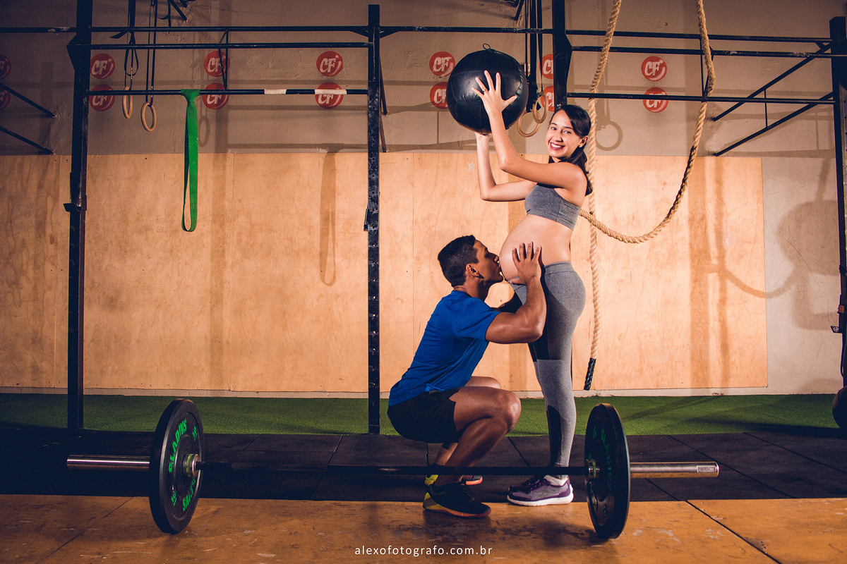 Casal fitness em ensaio de gestante. Lindas fotos de gestante na academia de crossfit. Casal jovem pousando para fotos de gestante por Alex Oliveira
