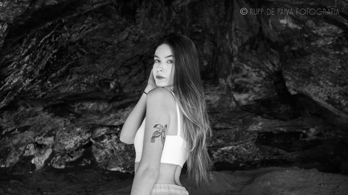 Isabella Moura em preto e branco na caverna do Morro da Mesa, de costas para a camera apenas olhando com o rosto.