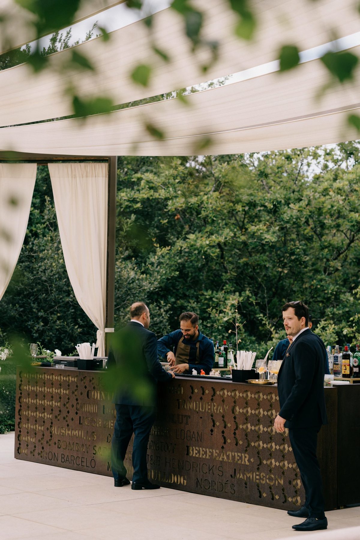 Bar exterior com bartenders a servir, sob toldo branco