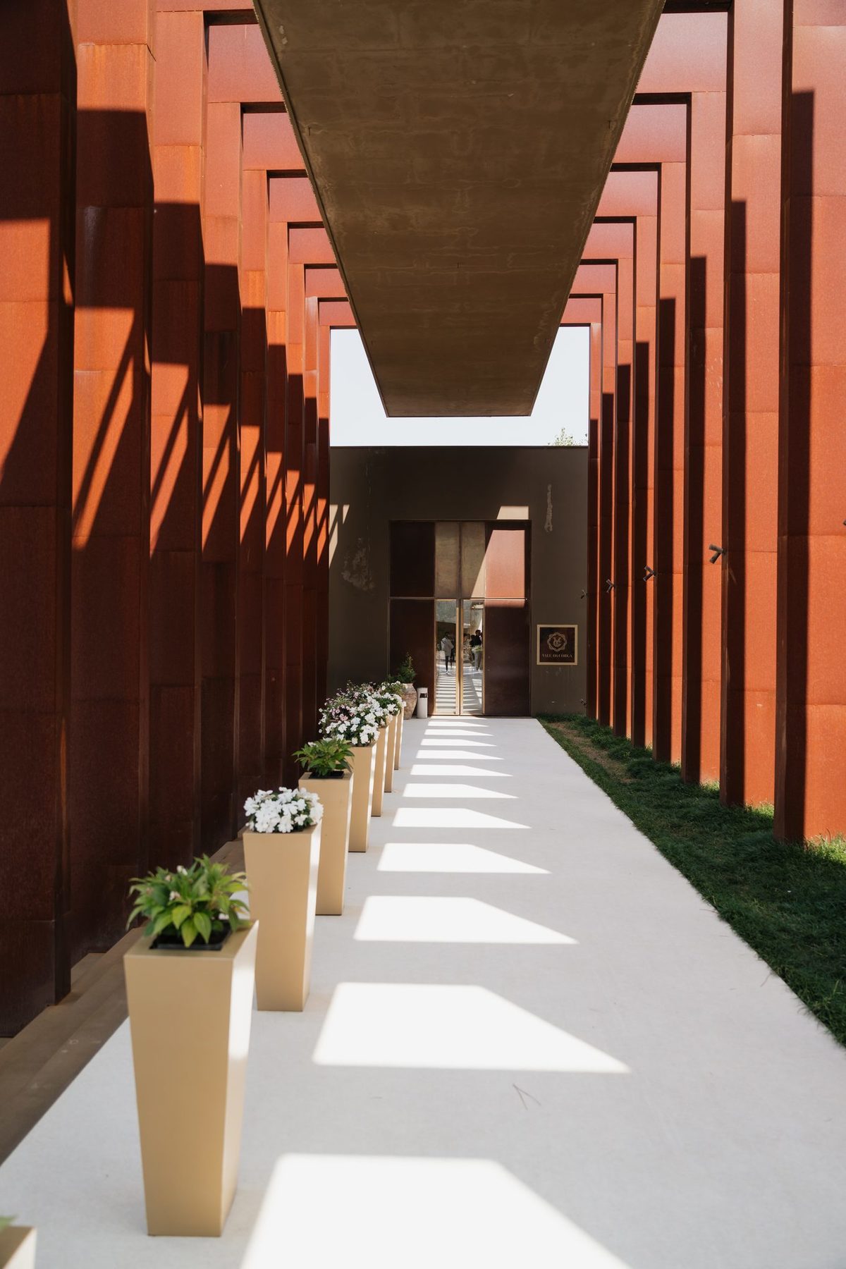 Corredor de entrada entre lâminas em aço corten, com vasos de flores