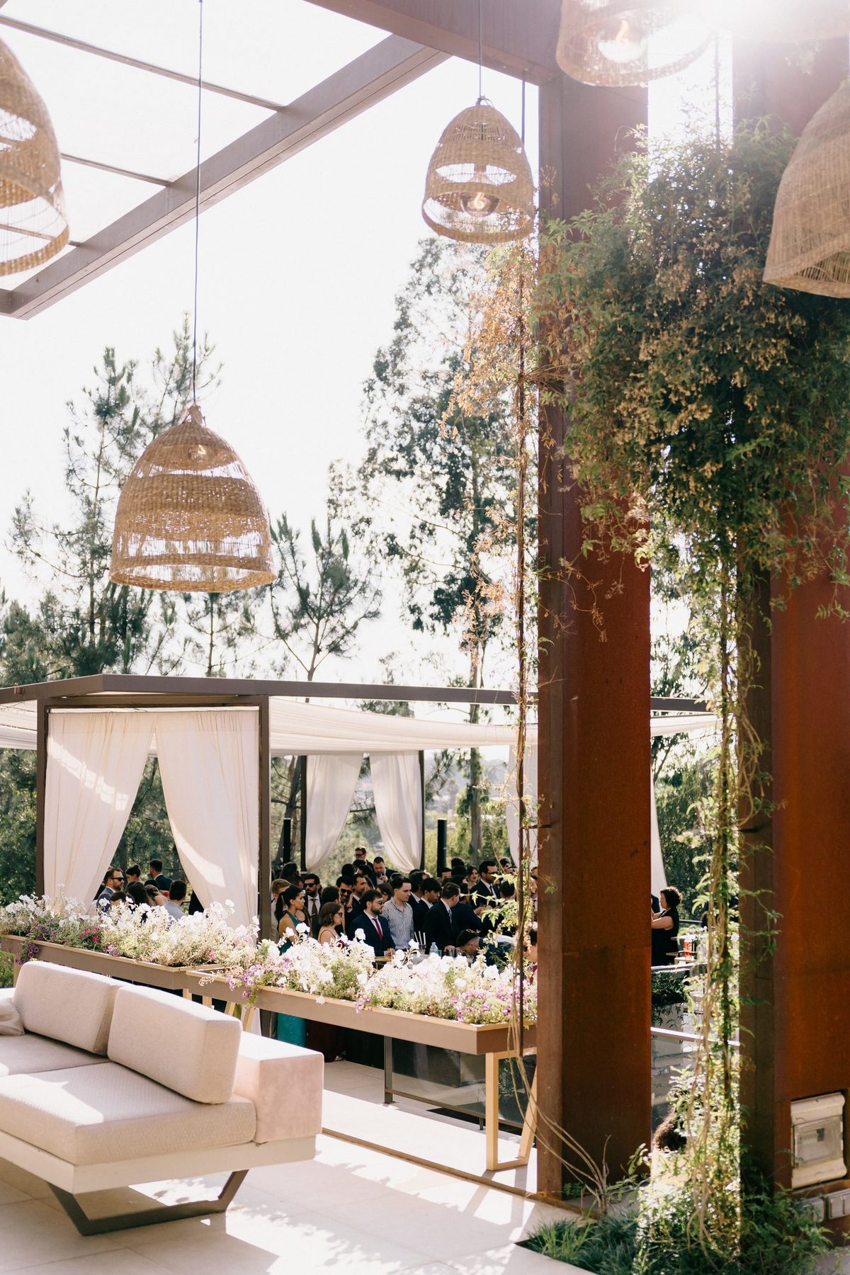 Pérgola exterior com candeeiros de vime, sofás e mesas decoradas