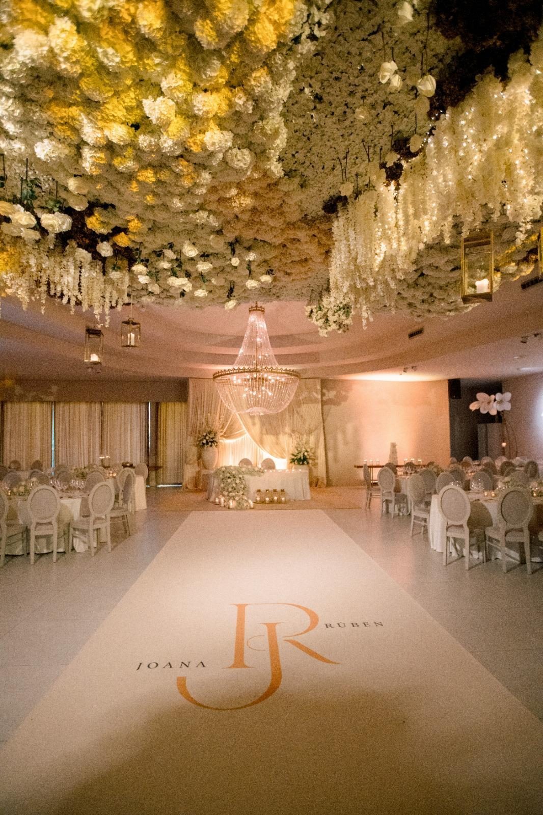 Sala principal com teto de flores, lustre e pista com monograma dos noivos