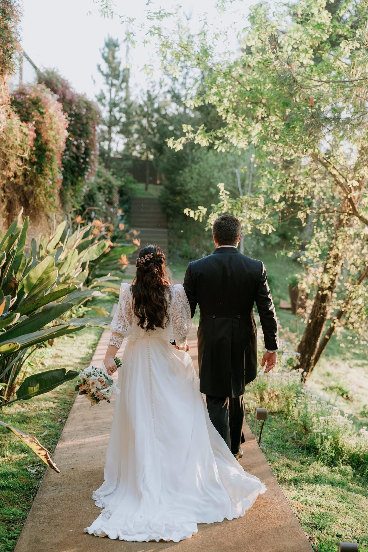 Noivos de costas a caminhar por um caminho do jardim